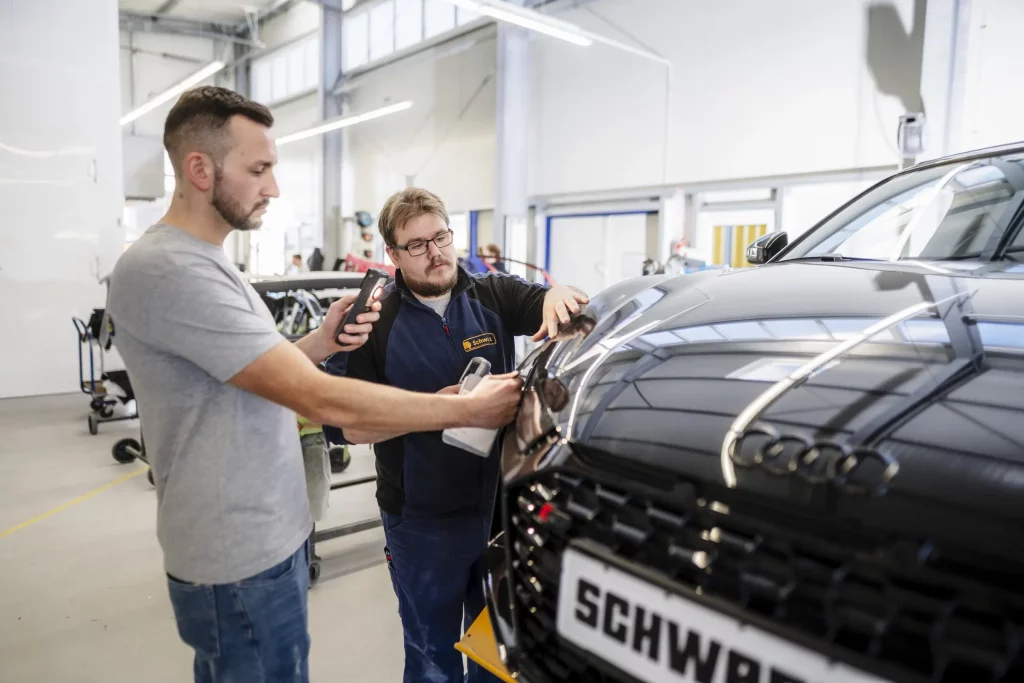 Werkstattmitarbeiter bei der Bestimmung des richtigen Farbtons für die fachgerechte Lackierung nach einem Unfallschaden.